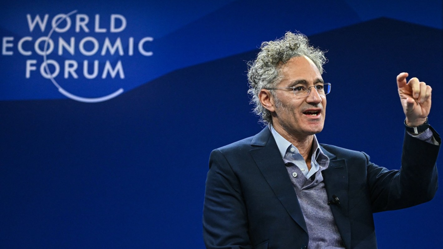 Palantir Technologies CEO Alex Karp gestures while speaking at the World Economic Forum against a blue backdrop.