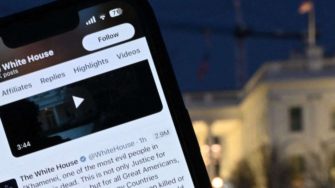 A smartphone displaying a tweet from the White House, with a blurred view of the White House in the background.