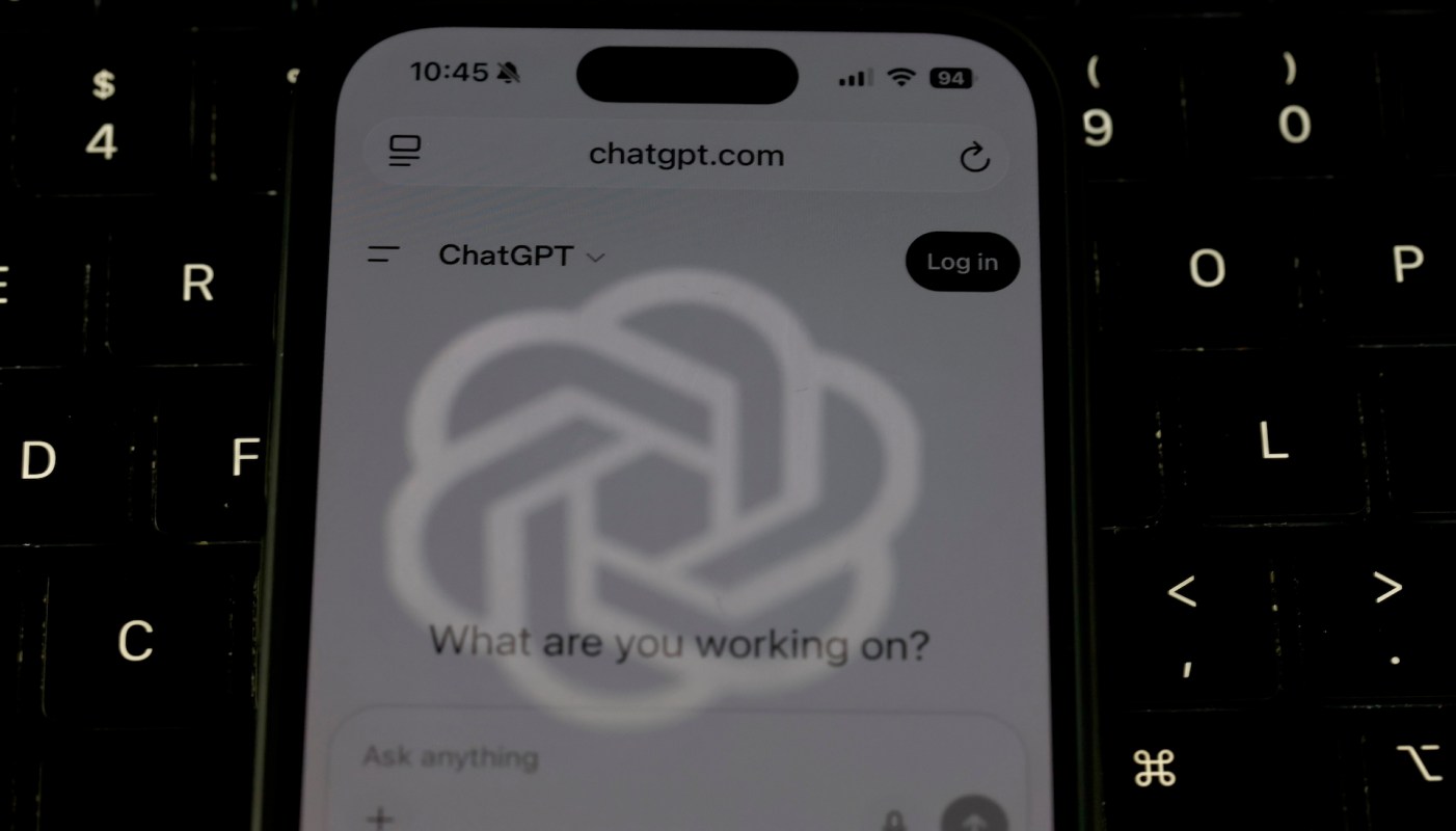A close-up of a smartphone displaying the ChatGPT website against a dark keyboard background.