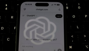 A close-up of a smartphone displaying the ChatGPT website against a dark keyboard background.