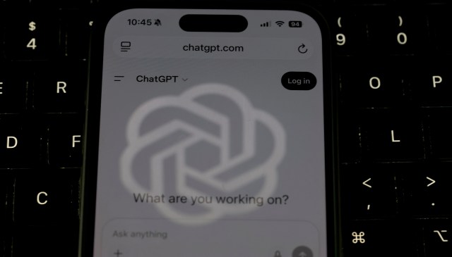 A close-up of a smartphone displaying the ChatGPT website against a dark keyboard background.