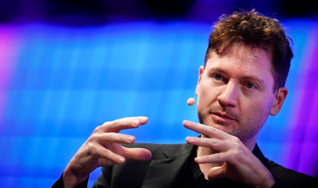 A man in a black jacket, tech mogul Bryan Johnson, speaks passionately with his hands in front of a blurred background.