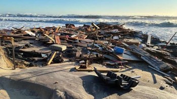 Debris from a storm, including wood and objects, scattered on a beach near crashing waves.