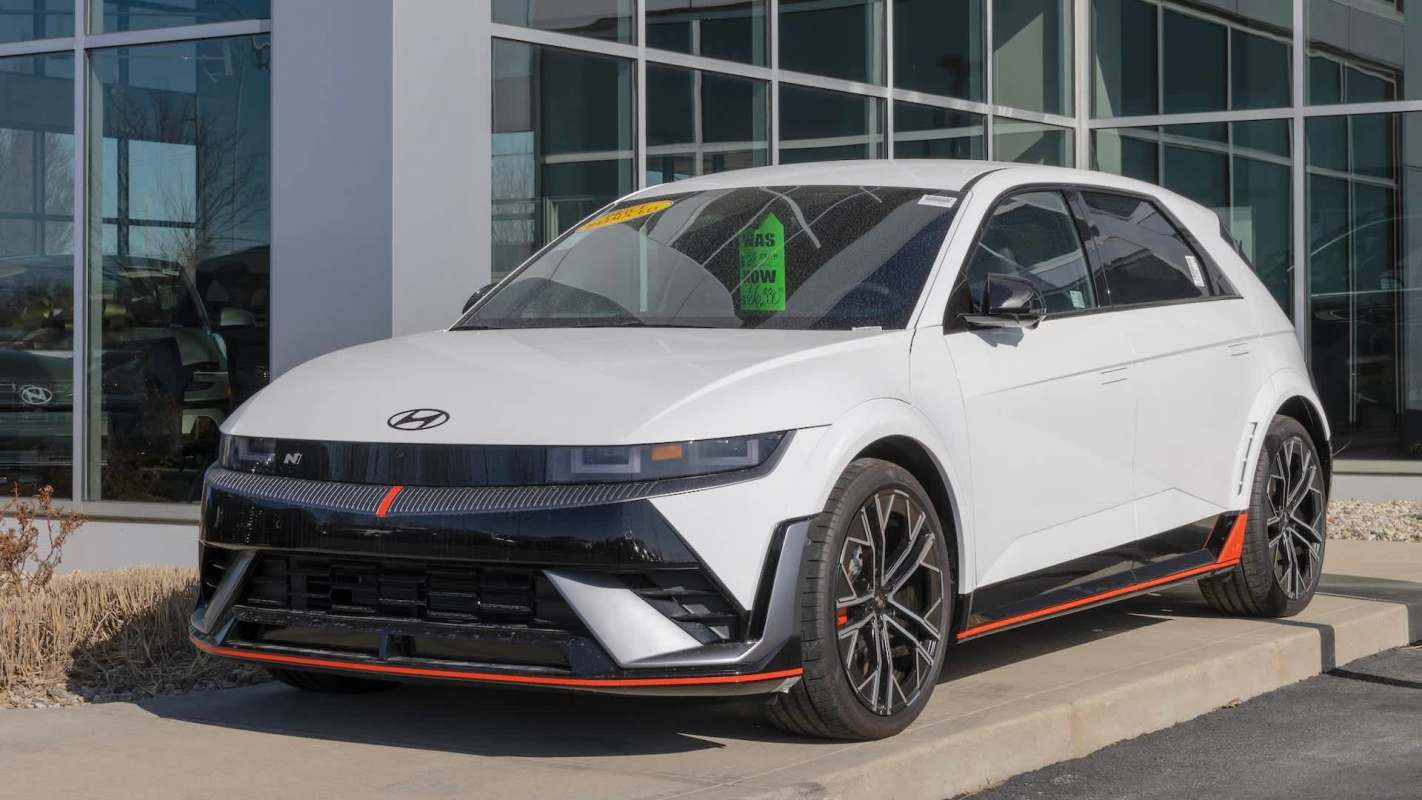 A sporty white Hyundai electric car displayed outside a dealership with a prominent 'Was Now' price tag in the window.