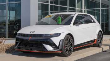 A sporty white Hyundai electric car displayed outside a dealership with a prominent 'Was Now' price tag in the window.