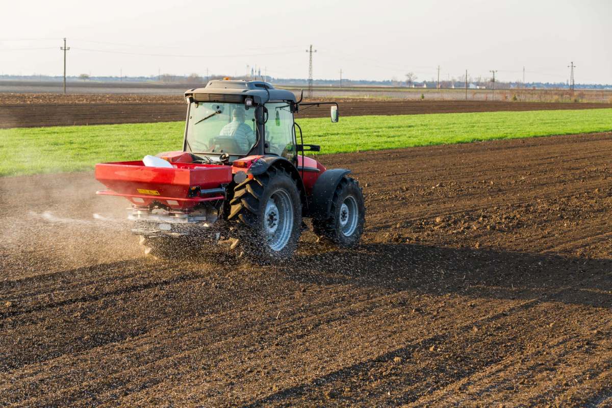 A tractor spreads fertilizer across a plowed field.