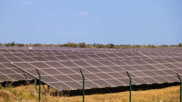 A large solar panel array stretches across a grassy landscape under a clear blue sky.