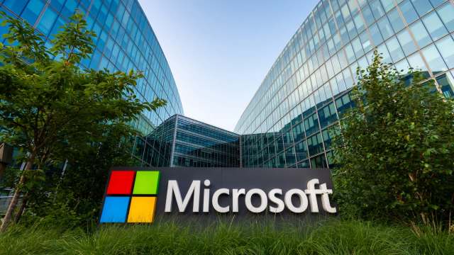 A Microsoft sign in front of modern glass office buildings surrounded by greenery.