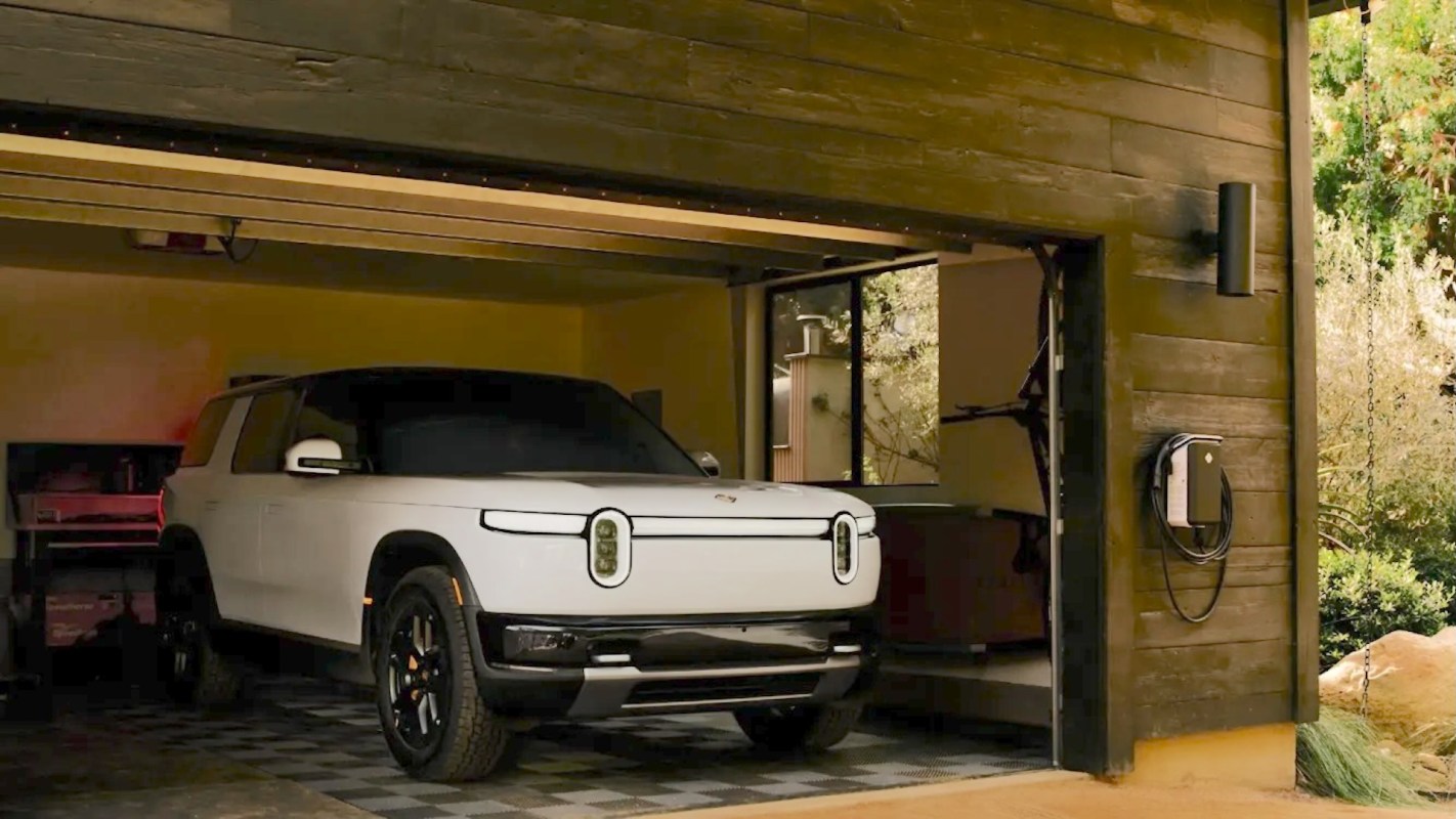 A white Rivian electric SUV parked inside a garage with a charging station.