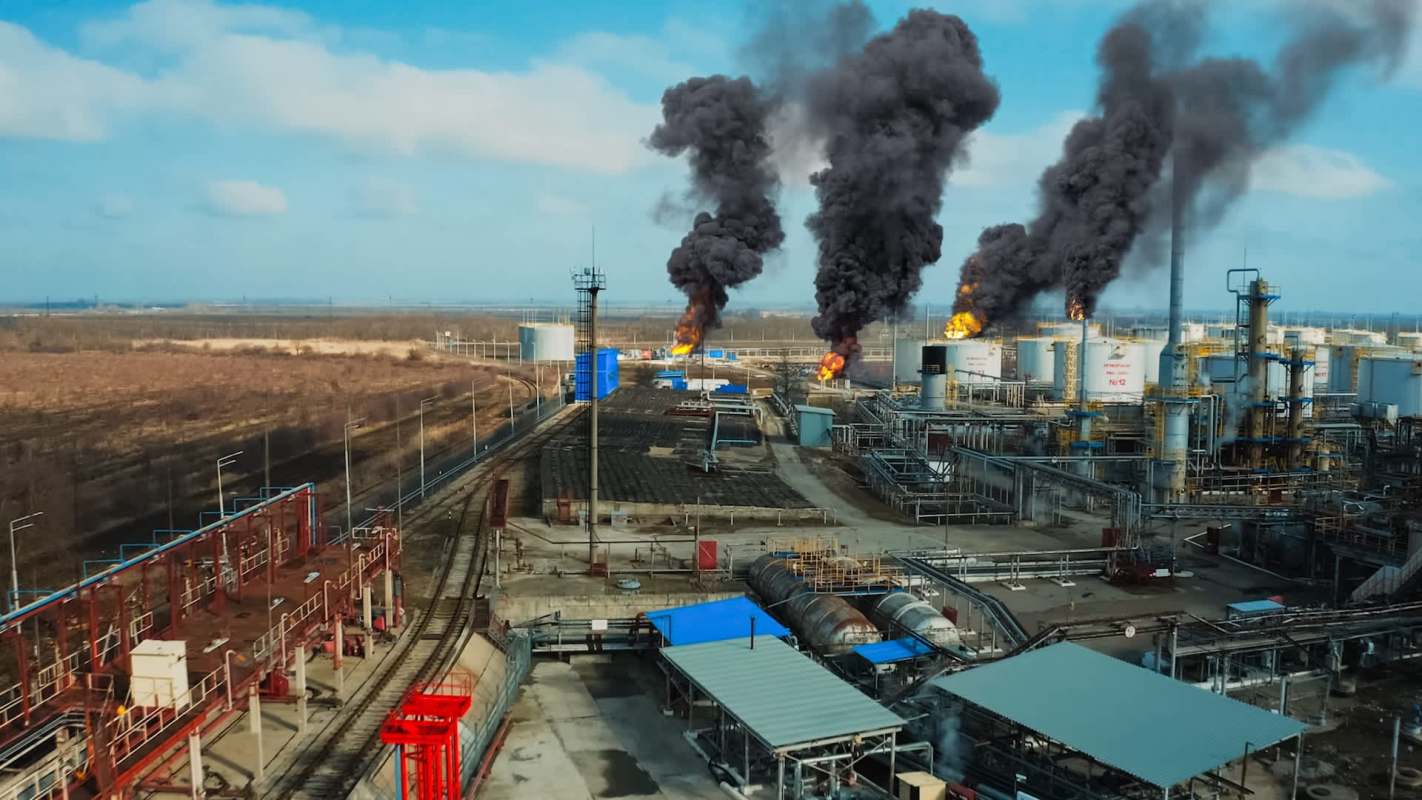 Aerial view of an industrial facility with flames and smoke rising from oil storage tanks.