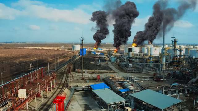 Aerial view of an industrial facility with flames and smoke rising from oil storage tanks.