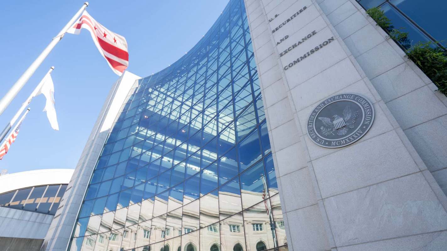 The U.S. Securities and Exchange Commission building with glass façade and flags against a clear blue sky.