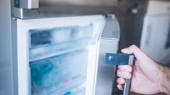 A hand gripping the handle of a stainless steel refrigerator door and opening it.
