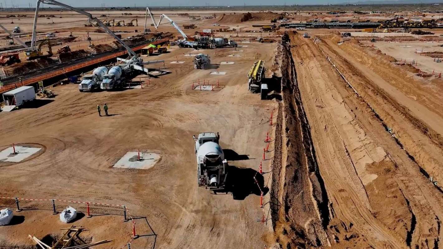 A construction site with heavy machinery, concrete mixers, and workers on a dusty landscape.