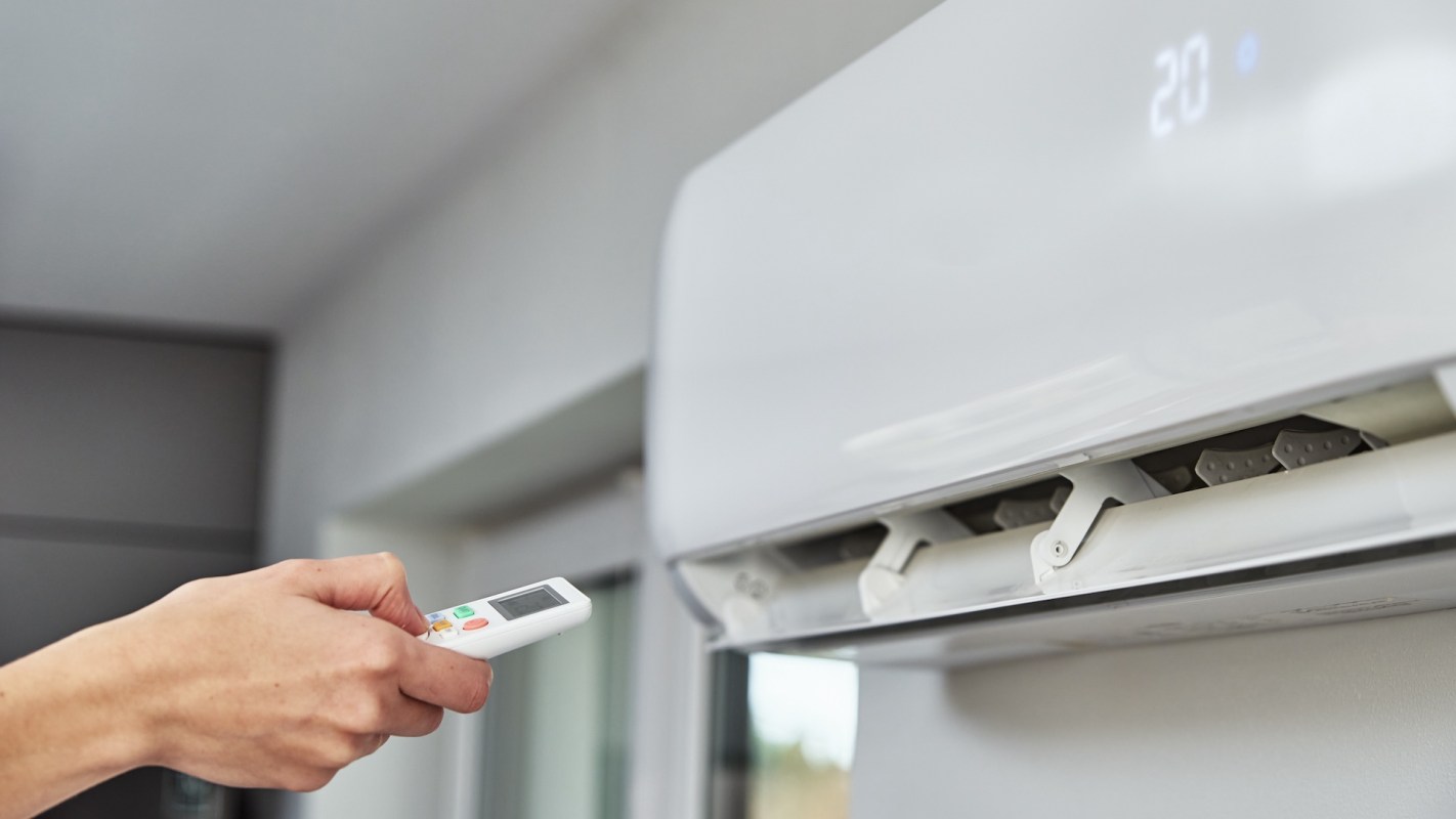 A person using a remote control to adjust a wall-mounted air conditioner displaying a temperature of 20°C.