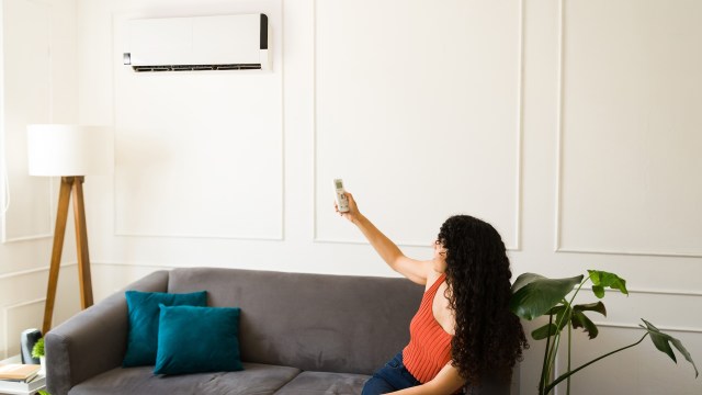 A woman sitting on a couch adjusts an HVAC with a remote.