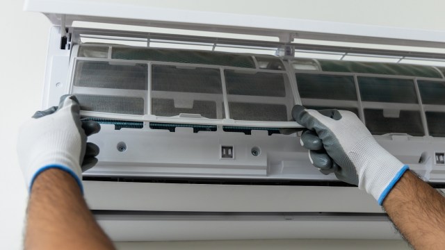 A person wearing gloves removes a filter from an air conditioning unit.