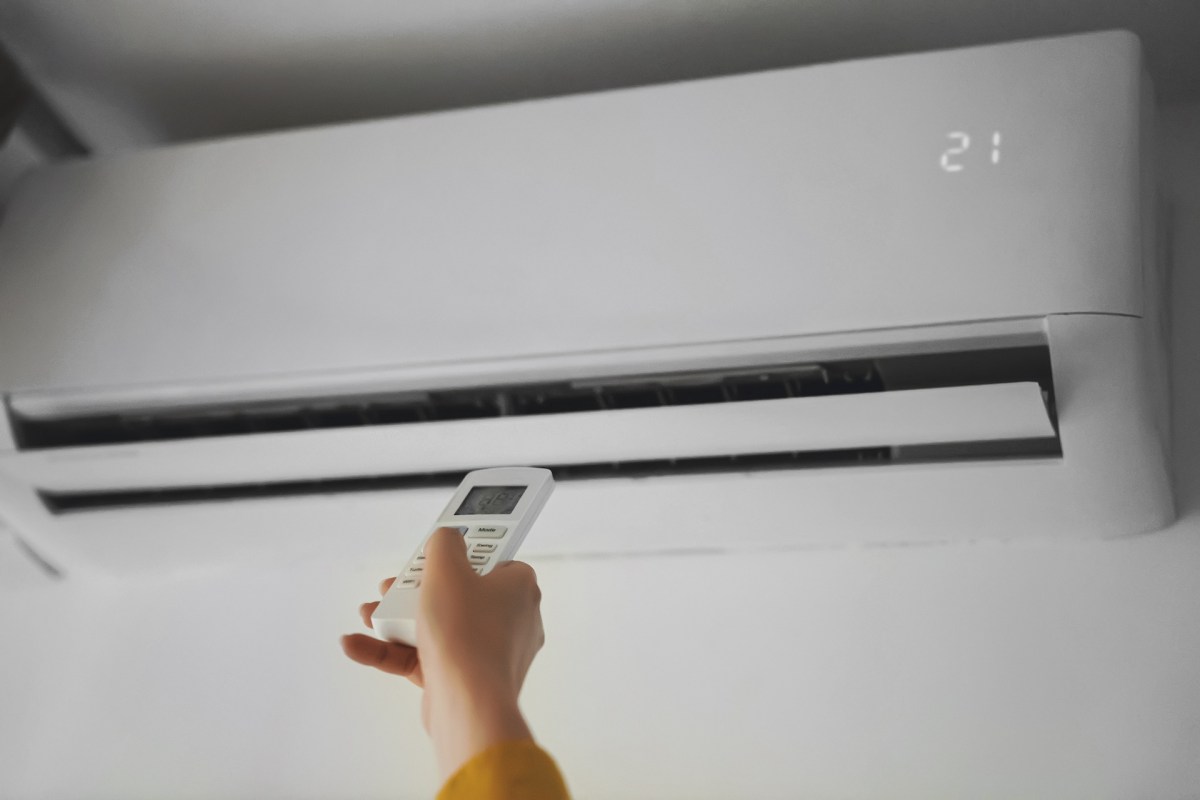 A person holding a remote control aimed at a wall-mounted air conditioner displaying the temperature.