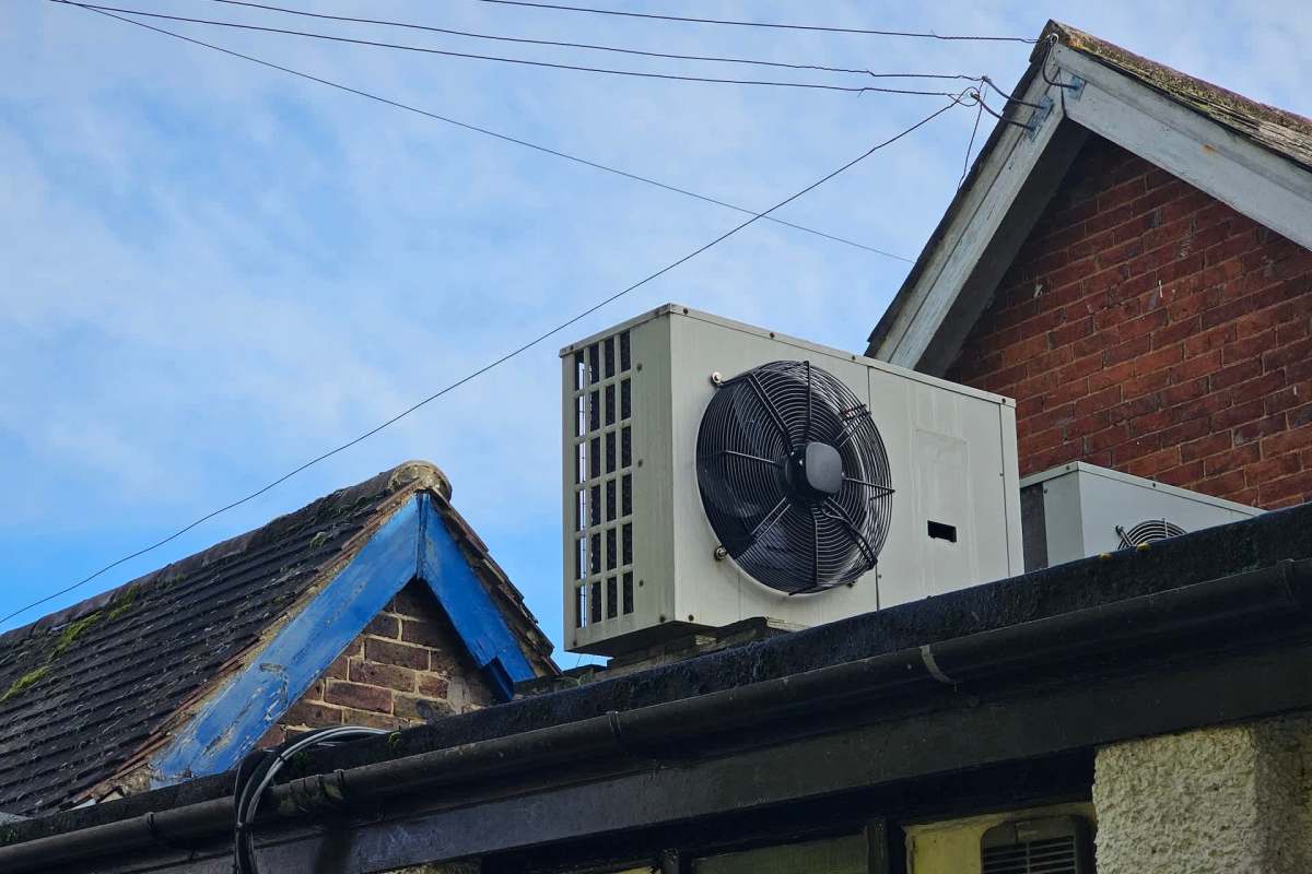 A heat pump mounted on the roof of a building under a clear blue sky.