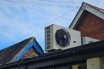 A heat pump mounted on the roof of a building under a clear blue sky.