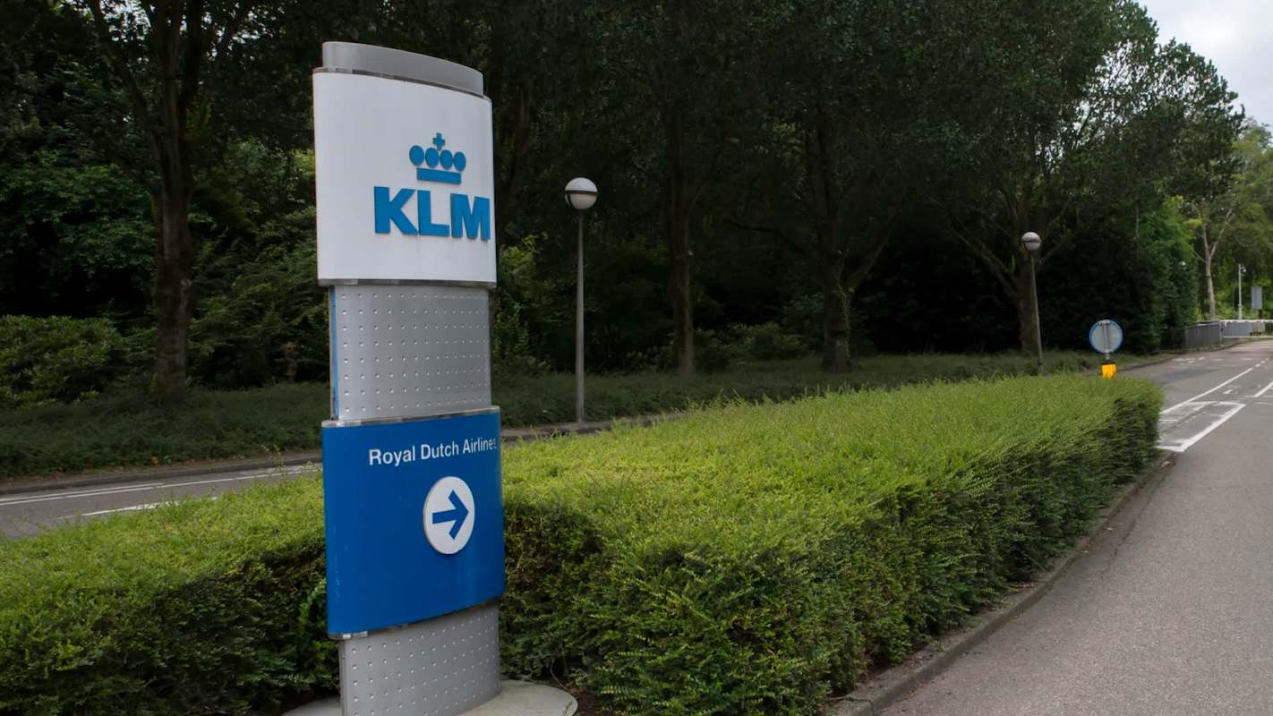 KLM sign indicating Royal Dutch Airlines, surrounded by greenery and a road leading away from it.