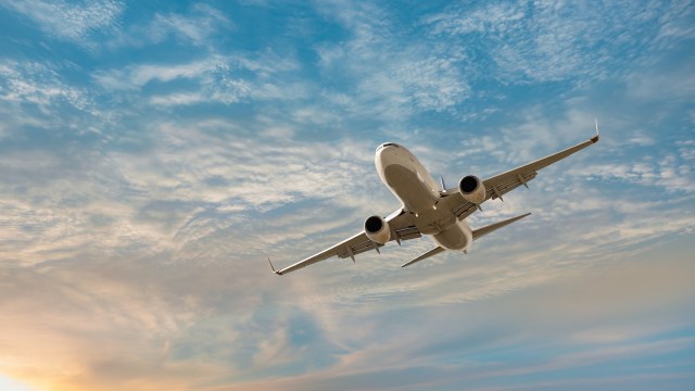 An airplane ascends into a blue sky filled with wispy clouds at sunset.