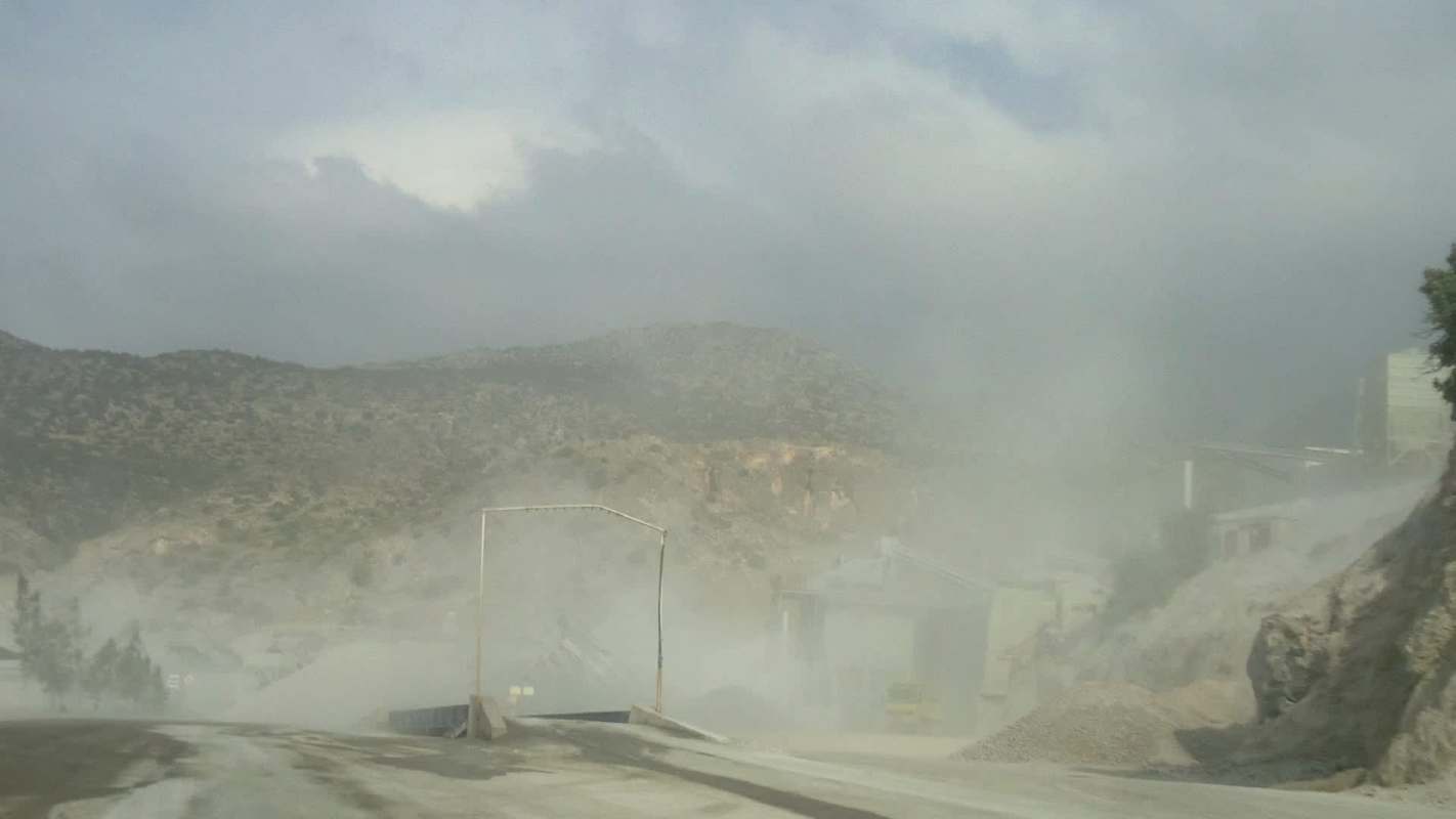 A dusty industrial site surrounded by mountains under a cloudy sky.