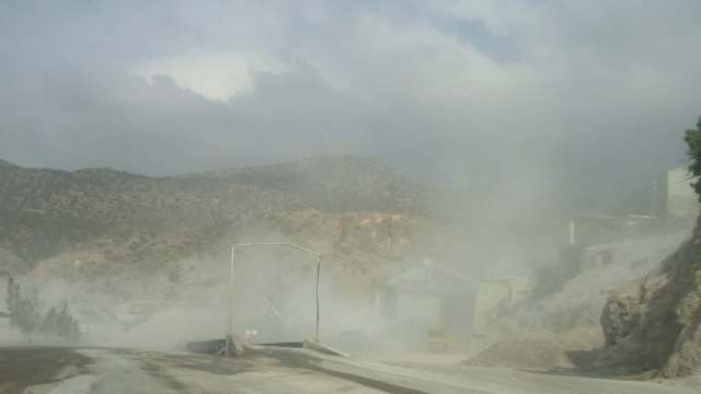 A dusty industrial site surrounded by mountains under a cloudy sky.