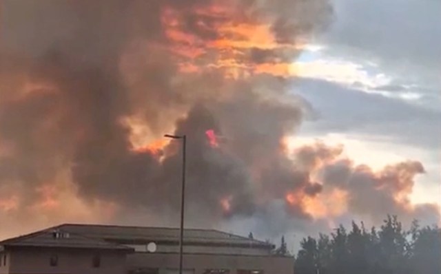 A dense plume of smoke billows into the sky, illuminated by orange and red hues from a nearby fire.