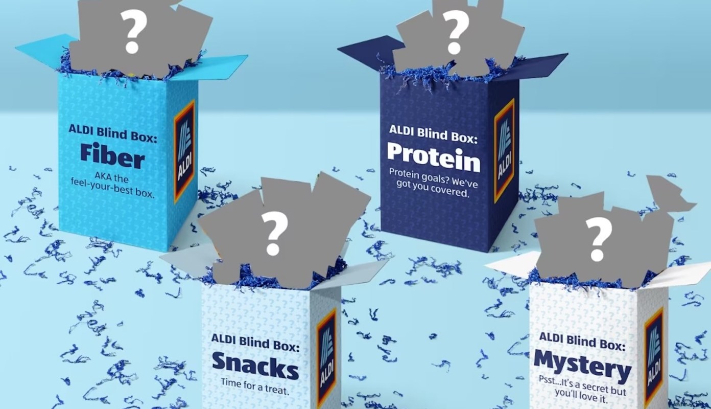 Four colorful Aldi-branded boxes labeled "Fiber," "Protein," "Snacks," and "Mystery" with gray question marks on top.
