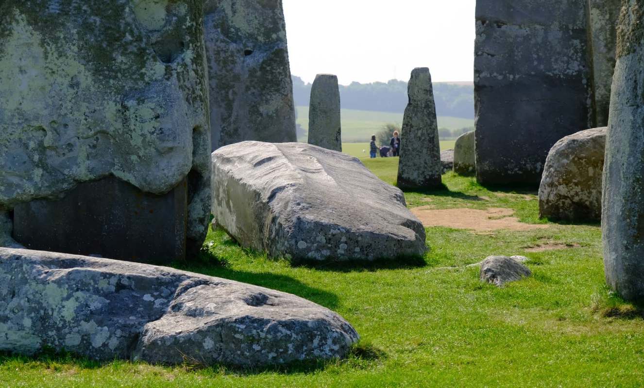 Stonehenge's ancient stones on green grass, with visitors in the background enjoying the historic site.