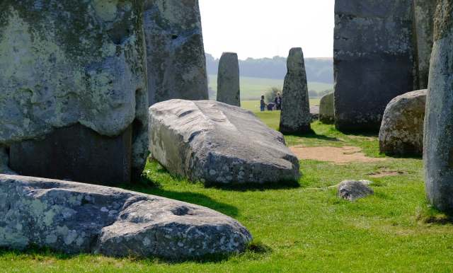 Stonehenge's ancient stones on green grass, with visitors in the background enjoying the historic site.