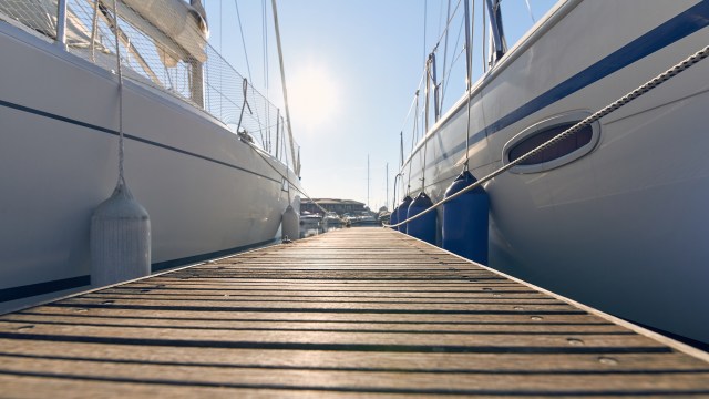 A wooden dock stretches between two sailboats under a bright sun on a clear day.