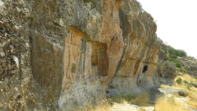 A rocky cliff with ancient carved niches and a dry landscape in the background.