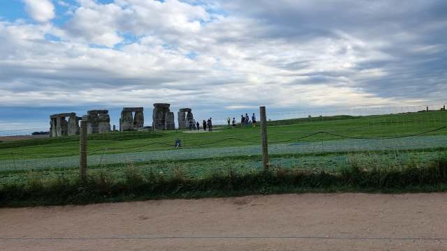 A group of visitors stands near the iconic stone structures of Stonehenge under a cloudy sky.