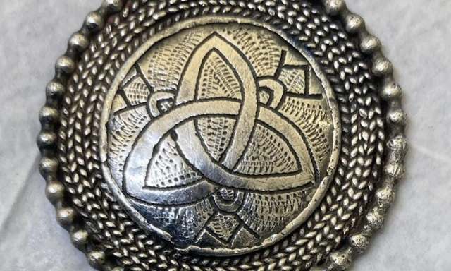 A circular silver pendant featuring an intricate Celtic knot design surrounded by a textured border.