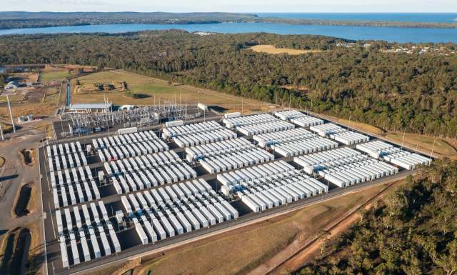 Aerial view of a large battery storage facility surrounded by trees and a body of water nearby.