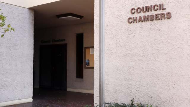 Entrance to a building labeled "Council Chambers," featuring a textured wall and nearby foliage.