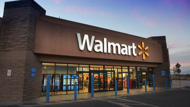 A Walmart store entrance with large signage and blue poles in the foreground, during twilight.