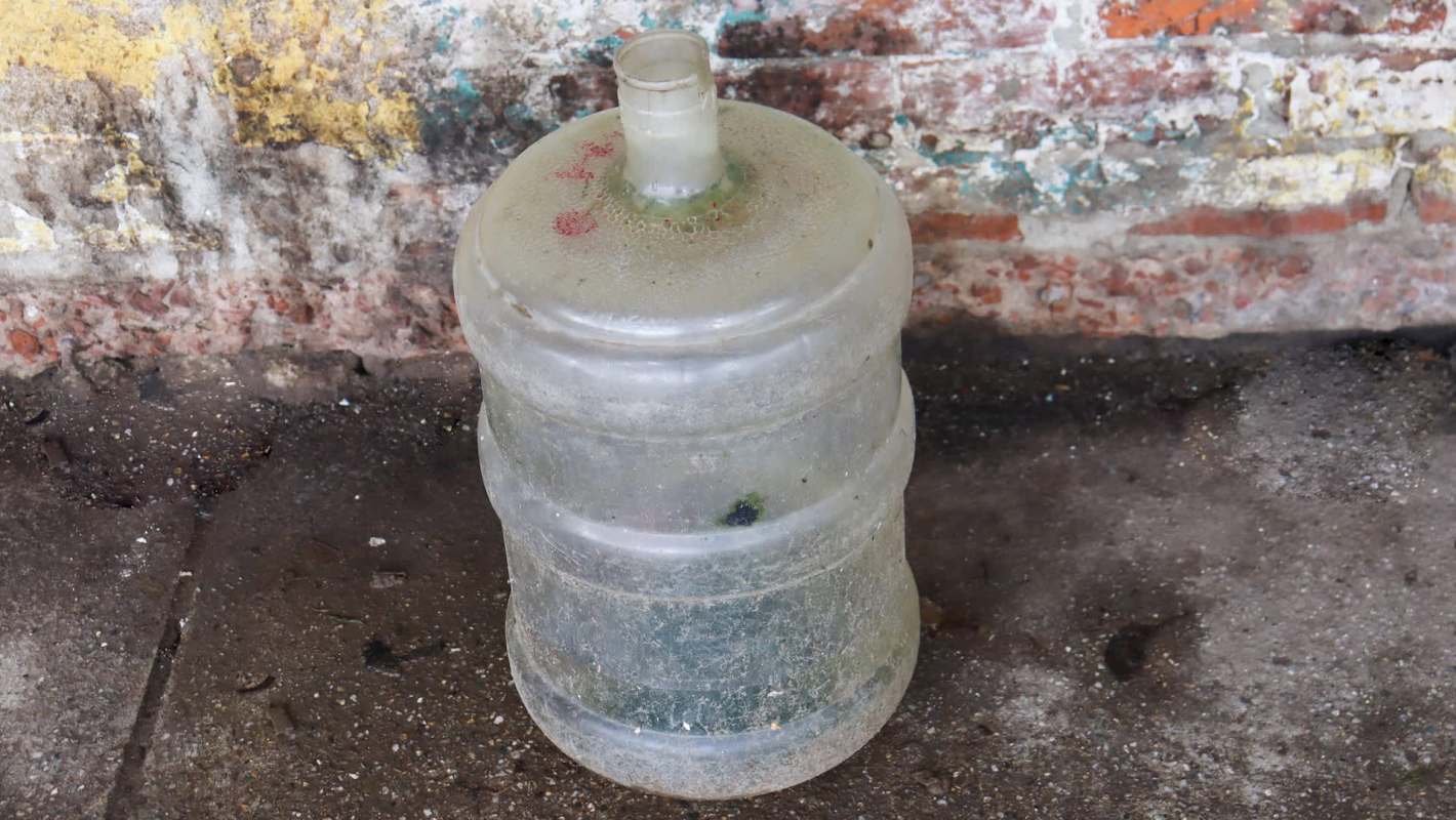 A dusty, empty plastic water bottle sits on a concrete surface against a weathered brick wall.