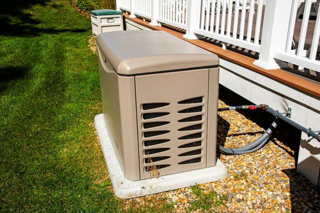 A generator unit sits on a concrete pad beside a house.