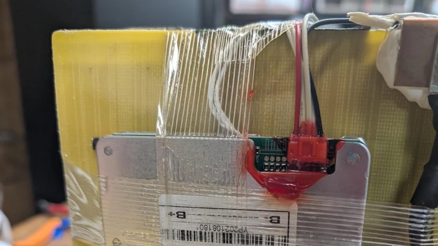 A close-up of a circuit board with wires, connectors, and a label, encased in plastic wrap.