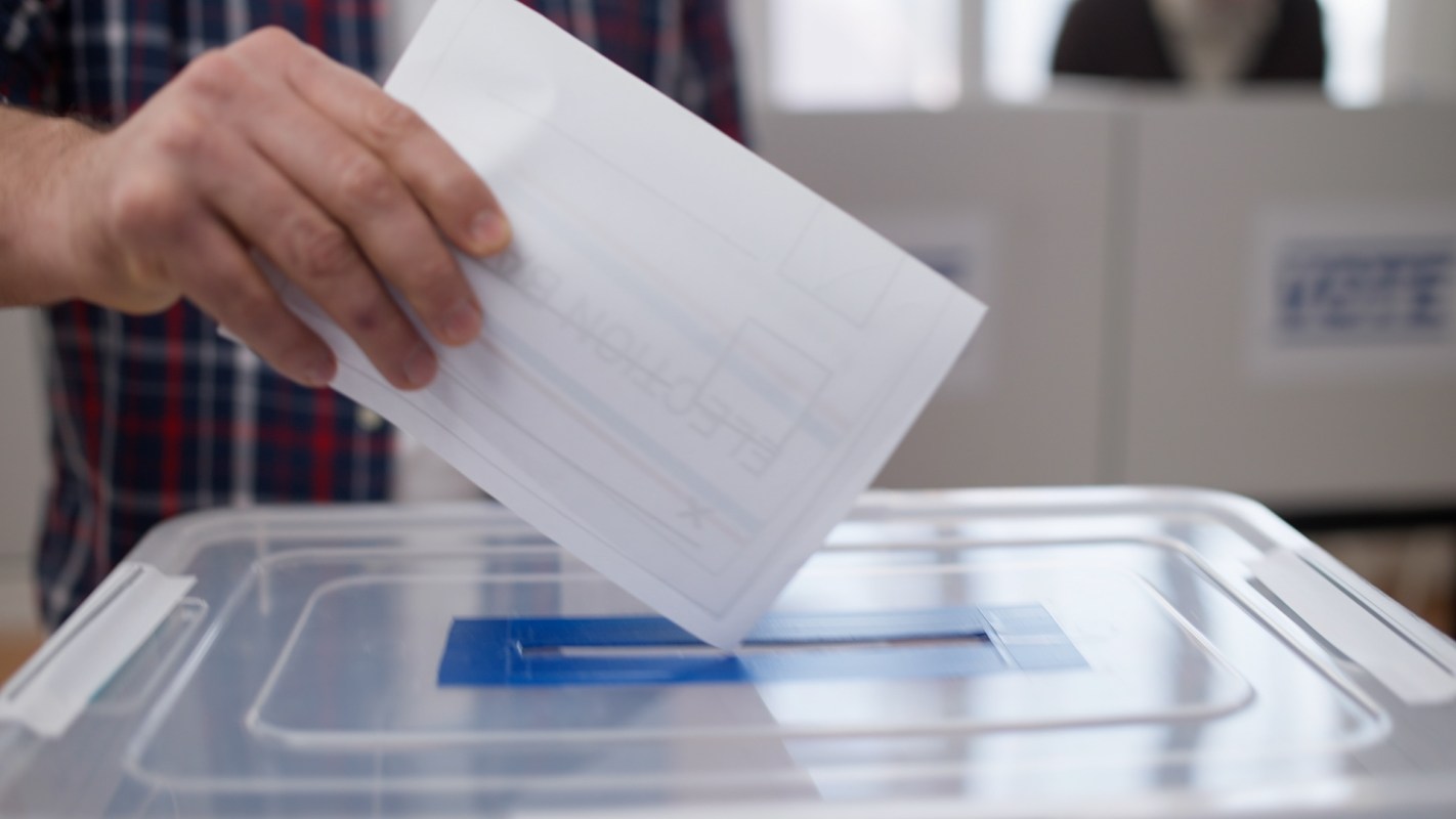 A person placing a ballot into a voting box.