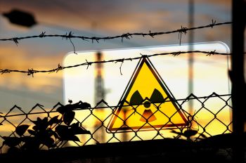 A yellow radiation warning sign behind the silhouette of barbed wire fencing.