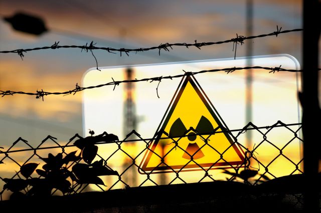 A yellow radiation warning sign behind the silhouette of barbed wire fencing.