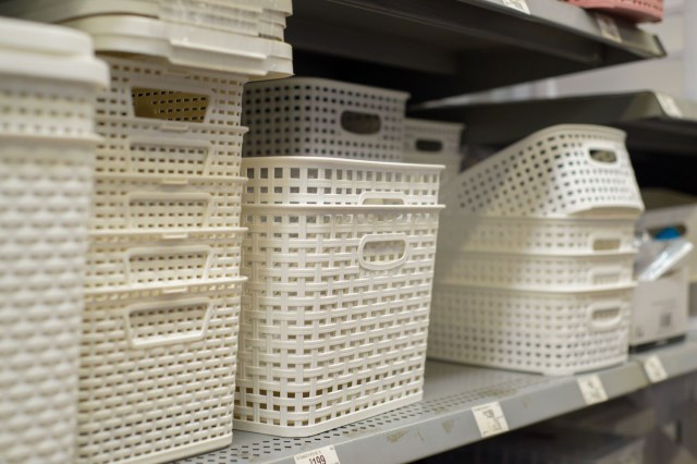 A display of various white plastic woven storage baskets stacked on a retail shelf.