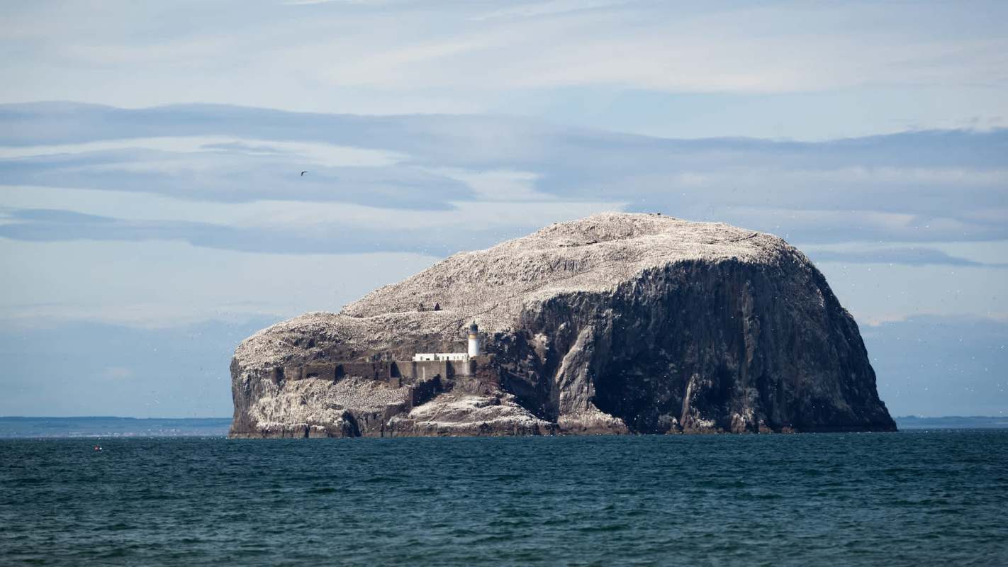 A rocky island with a lighthouse surrounded by water and a cloudy sky in the background.