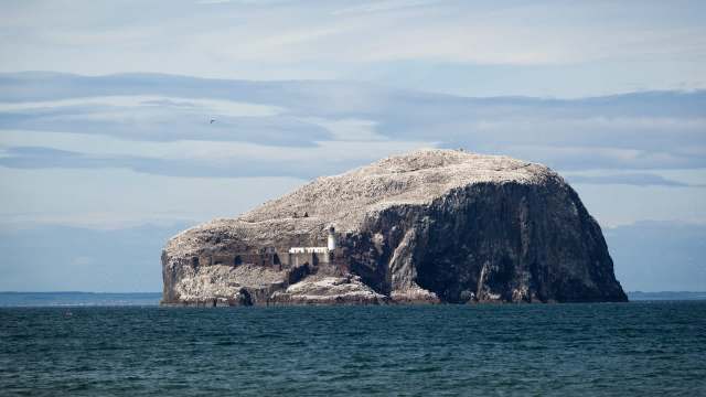 A rocky island with a lighthouse surrounded by water and a cloudy sky in the background.