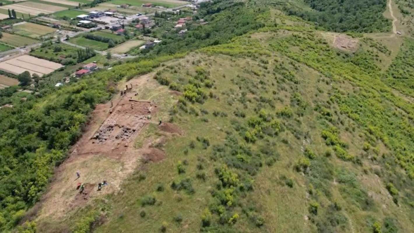 An archaeological dig site on a hillside surrounded by green vegetation and farmland.