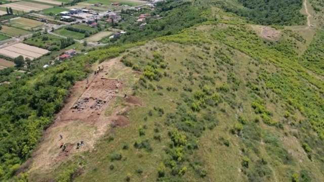 An archaeological dig site on a hillside surrounded by green vegetation and farmland.